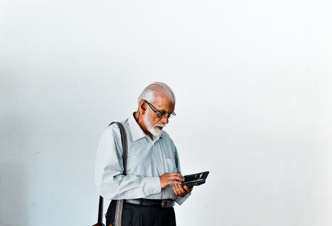 En äldre herre med glasögon tittar på sin smartphone.